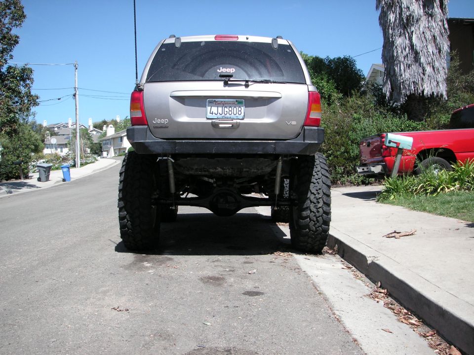 Silver 1999 Jeep Grand Cherokee with lifted suspension and oversized tires, viewed from the rear