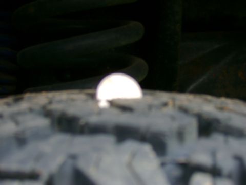 1989 Ford Bronco - A close-up view of a vehicle's tire and suspension system, with a bright reflection on the tire's surface.
