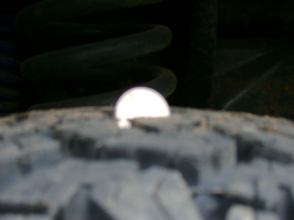 Close-up of a tire tread with a bright reflection and a dark suspension spring behind it
