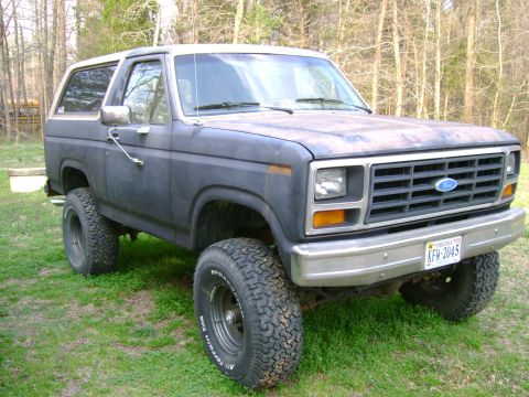 1989 Ford Bronco - This 1980s Ford Bronco is shown from a three-quarter front angle, with its distinctive grille and off-road tires clearly visible.
