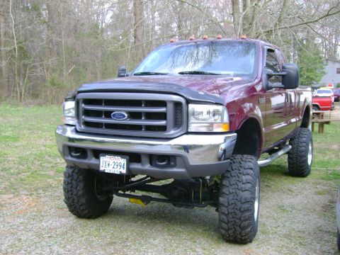 1989 Ford Bronco - This lifted Ford F-250 Super Duty pickup truck is shown from a three-quarter front angle, with a red truck visible in the background.
