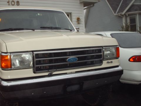 1990 Ford Bronco - Close-up of a 1990 Ford Bronco's front grille and headlights, with another vehicle visible to the right.