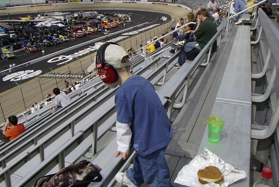 Spectators in bleachers watch a race track with many cars lined up