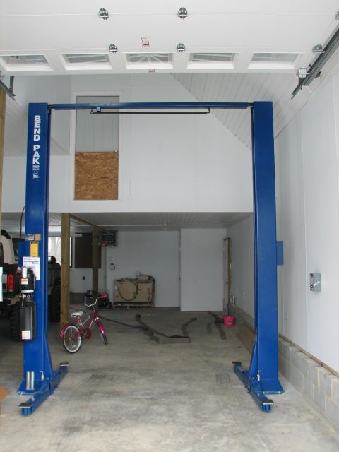 1992 Ford Bronco - A blue car lift stands in the center of a garage, with a pink bicycle to its left.