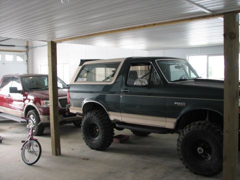 1992 Ford Bronco - A lifted 1992 Ford Bronco is parked inside a garage next to a red pickup truck and a child's bicycle.