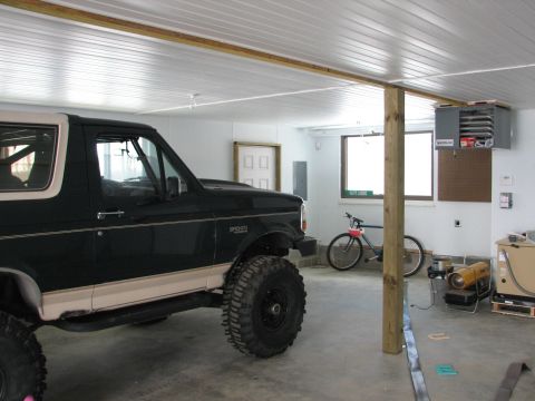 1992 Ford Bronco - A dark green 1992 Ford Bronco with beige trim and large tires is parked inside a garage.