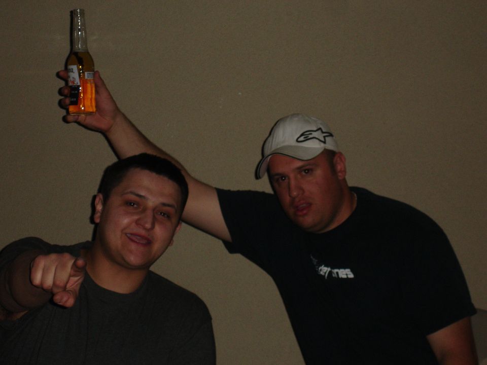 Two men pose for a photo, one holding a beer bottle above his head