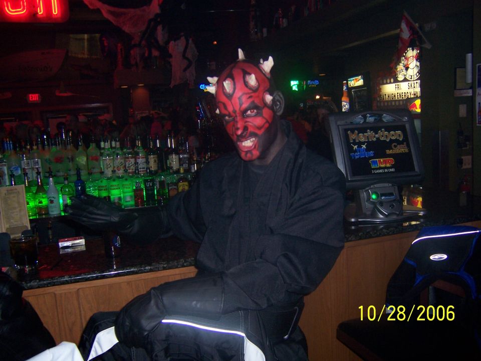 Person in Darth Maul costume at a bar with bottles and a game machine