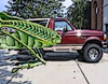 1989 Ford Bronco - Side profile of a maroon 1989 Ford Bronco parked on pavement, partially hidden by large green leaves.