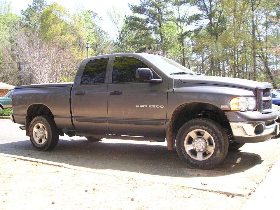 Passenger side view of a dark gray Dodge Ram 2500 Hemi quad cab pickup parked on gravel near trees