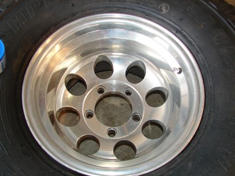 1996 Ford Bronco - Head-on close-up of a freshly polished eight-hole deep-dish aluminum wheel on a mounted radial tire, lying flat on the ground with no cente…