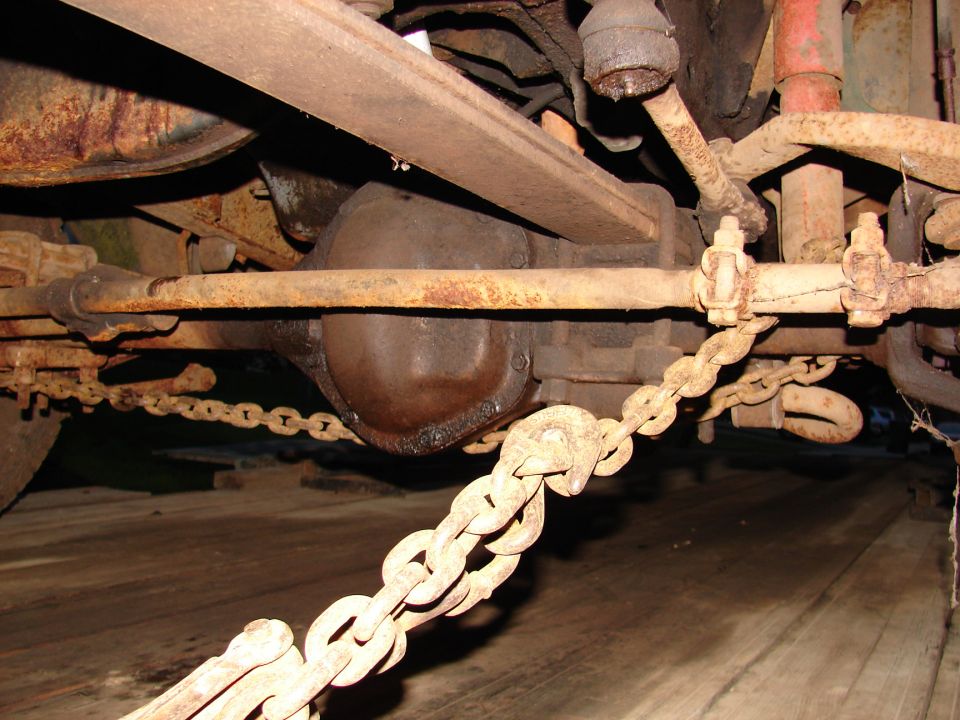 Underside view of a rusty solid axle and leaf spring with a chain wrapped around