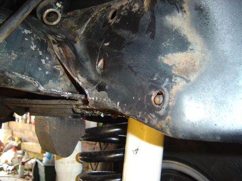 1986 Ford Bronco - Close-up of a rusty, oil-stained black steel frame section with two threaded bolt holes and a visible crack near a welded seam. Below sits…