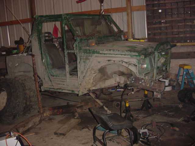 Green off-road vehicle chassis on jack stands, front end removed, in a workshop