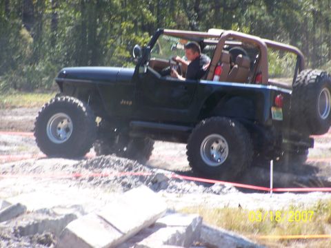 1989 Ford Bronco - A black Jeep Wrangler navigates an off-road course with large tires and a roll cage visible.