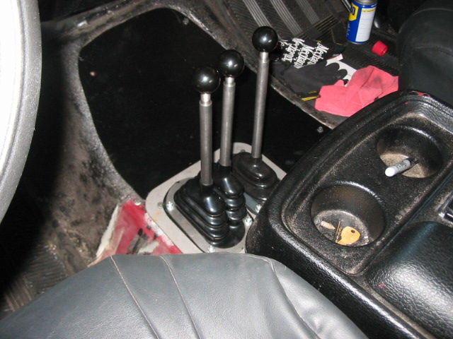 Interior shot of a vehicle's center console showing three gear shifters and cup holders with a key inside