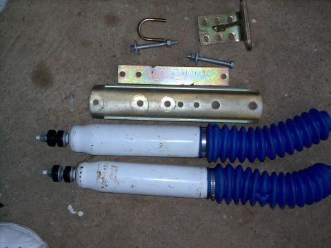 1982 Ford Bronco - Various automotive parts, including shock absorbers and metal brackets, are laid out on a concrete floor.