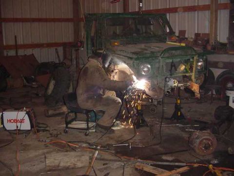 1992 Ford Bronco - Welding repairs are underway on the front section of a green vehicle inside a workshop.