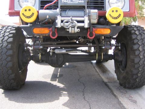 1987 Suzuki Samurai - Close-up view of the front axle, winch, and distinctive yellow "Daylighter" lights on an off-road vehicle.