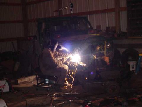 1992 Ford Bronco - A person is welding on a vehicle frame in a dimly lit workshop.