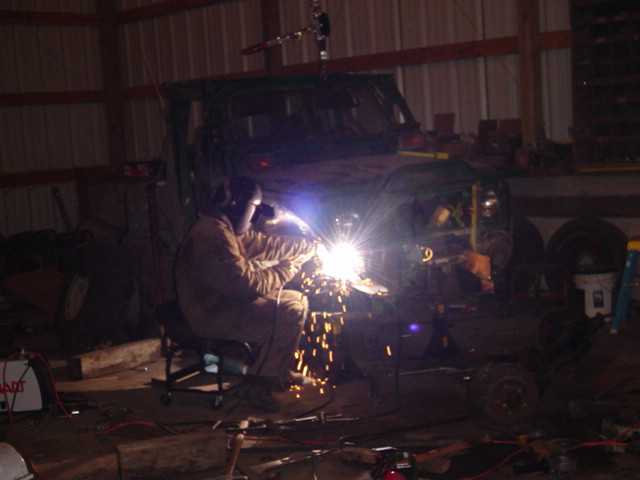 Person welding on the side of a vehicle chassis inside a barn