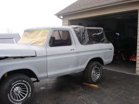 1979 Ford Bronco - Side view of a Ford Bronco undergoing bodywork, with a black soft top and primer finish.