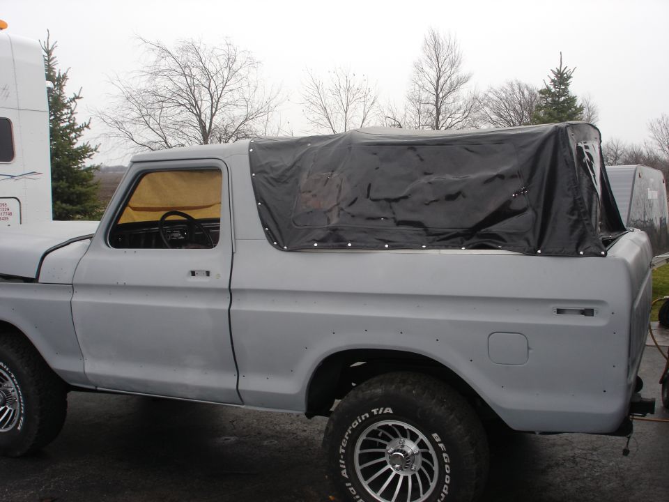 Gray Ford Bronco with a black soft top, side view. It's sitting next to a white trailer