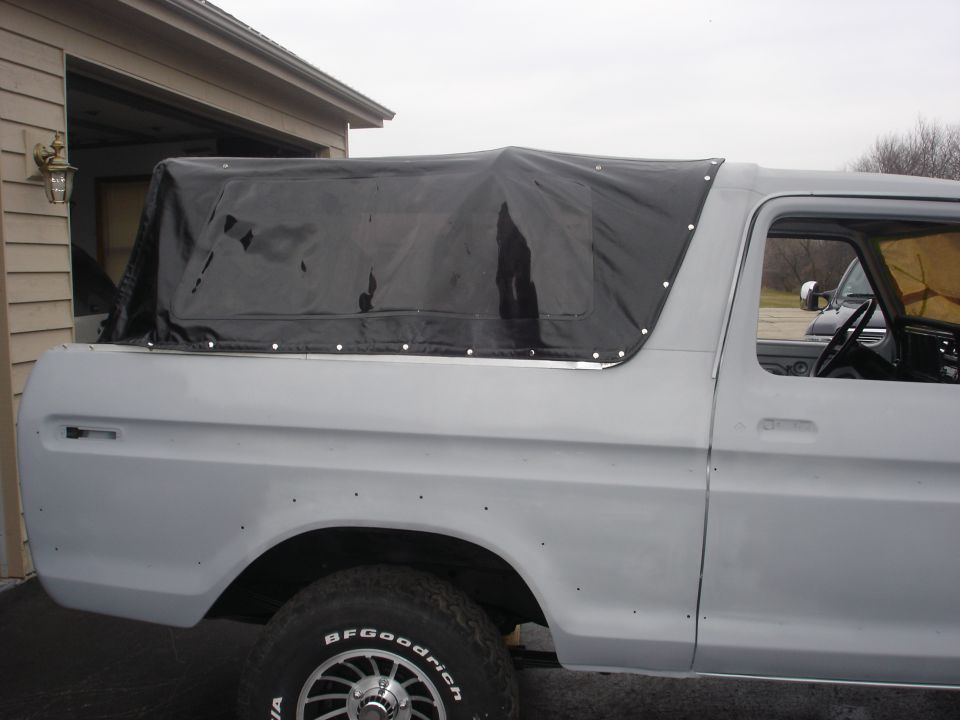Gray Ford Bronco with a black soft top, side view, showing the rear fender and wheel