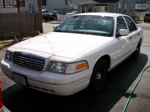 1999 Ford Crown Victoria - A white sedan, possibly a Ford Crown Victoria, is parked outdoors on a sunny day.