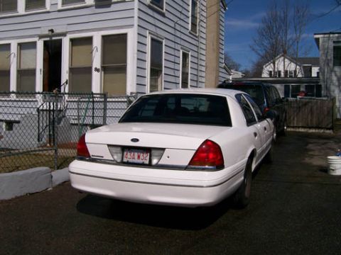 1999 Ford Crown Victoria - A white Ford Crown Victoria is parked in a driveway next to a dark SUV.
