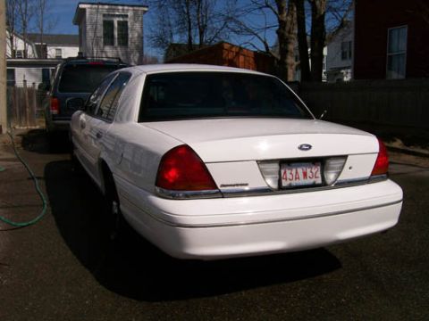 1999 Ford Crown Victoria - The rear of a white 1999 Ford Crown Victoria is visible, its distinctive taillights and license plate.