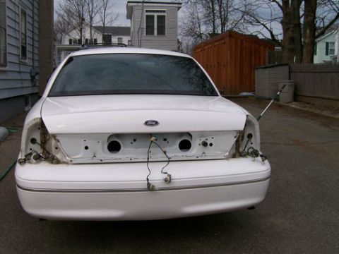 1999 Ford Crown Victoria - Rear view of a white Ford Crown Victoria undergoing repairs or modifications, with its bumper and taillights removed.