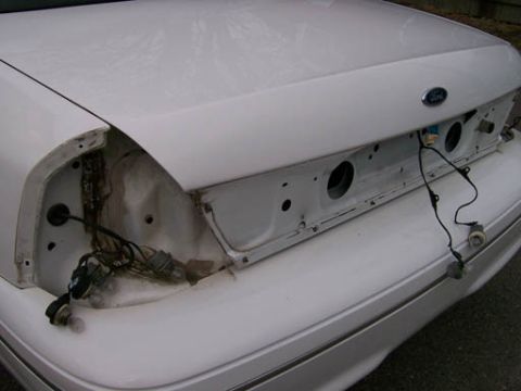 1999 Ford Crown Victoria - The rear of a white Ford Crown Victoria is shown with its taillights removed, exposing the internal wiring and trunk compartment.