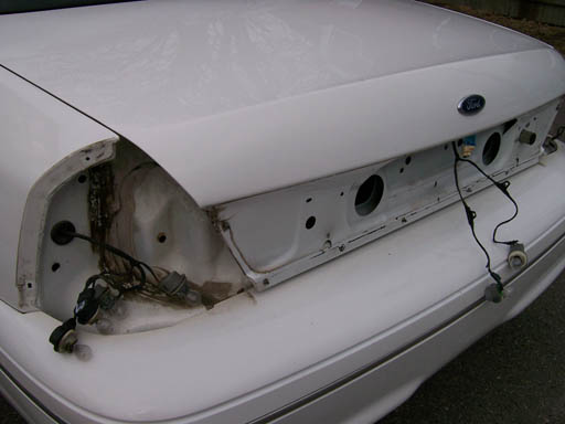 Rear of a white Ford Crown Victoria with taillights removed, showing wiring and trunk area
