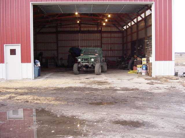 Green off-road vehicle with large tires parked inside a red barn
