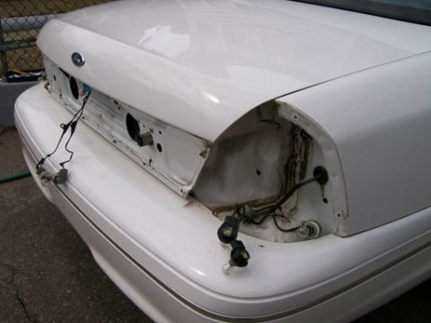 1999 Ford Crown Victoria - Rear view of a white 1999 Ford Crown Victoria with its taillights removed, showing exposed wiring and trunk area.