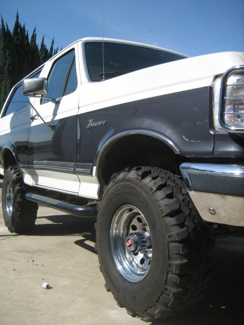 1989 Ford Bronco - A low three-quarter front view of a lifted full-size Ford Bronco painted two-tone charcoal-gray over white, with a chrome grille guard and…
