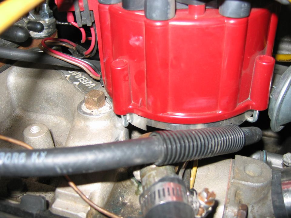 Red engine distributor cap with wires and a ribbed hose. Text 'WEIAN' is visible on a metal part