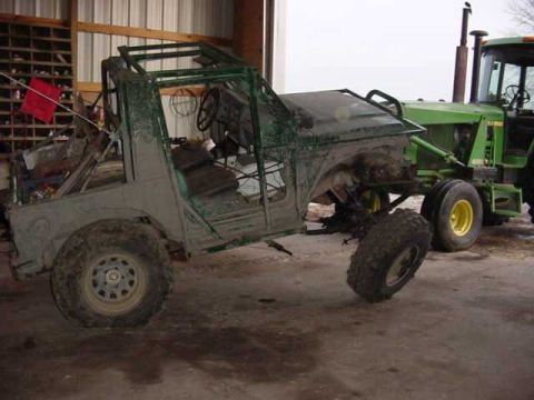 1992 Ford Bronco - An off-road vehicle, appearing to be a project or custom build, is parked next to a large green tractor in a barn.