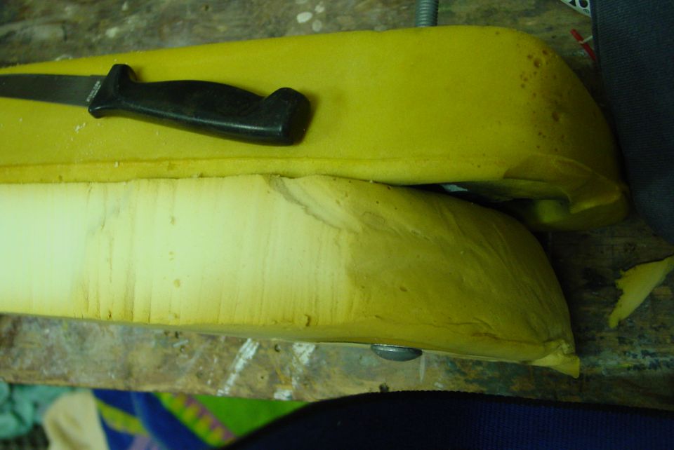Yellow seat foam bolsters being trimmed with a knife on a workbench