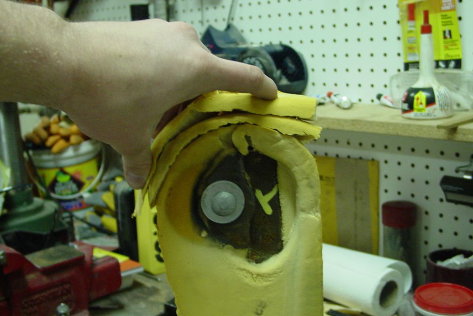 Yellow foam armrest pad held open to show exposed mounting bolt in a workshop