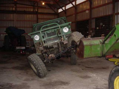 1992 Ford Bronco - This green off-road vehicle has large tires and a front brush guard, and is parked inside a building.