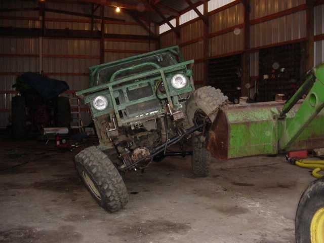 Green off-road vehicle with large tires and a front brush guard, parked indoors