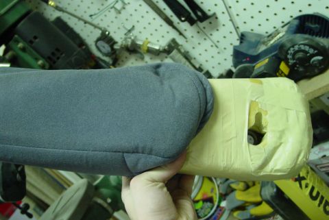 1993 Ford Bronco - A gray fabric arm rest, wrapped in yellow tape, is held by a person's hand in a workshop.
