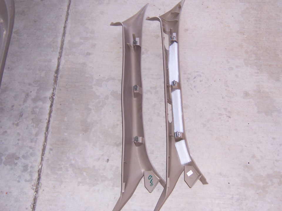 Pair of tan A-pillar interior trim panels on concrete, showing clips and foam padding