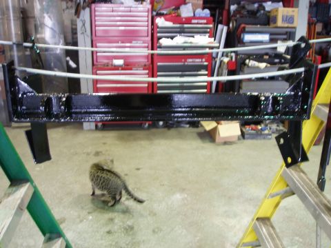 1979 Ford Bronco - A freshly painted vehicle frame part is suspended in a workshop setting.