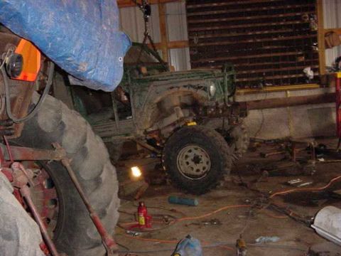 1992 Ford Bronco - A green off-road vehicle is suspended by a crane in a workshop, undergoing repairs or modifications.