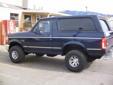 1995 Ford Bronco - A dark blue 1995 Ford Bronco is parked outside a building with a Coca-Cola machine.