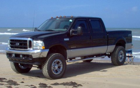 1995 Ford Bronco - A four-door Ford pickup truck is parked on the beach with the ocean in the background.