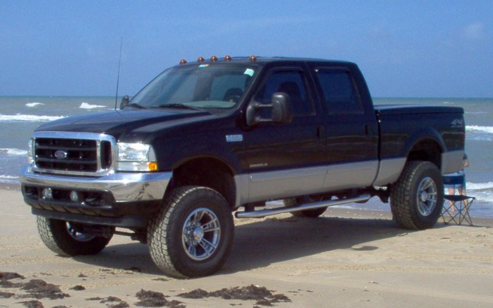 Black and silver Ford F-250 pickup truck parked on a sandy beach near the ocean